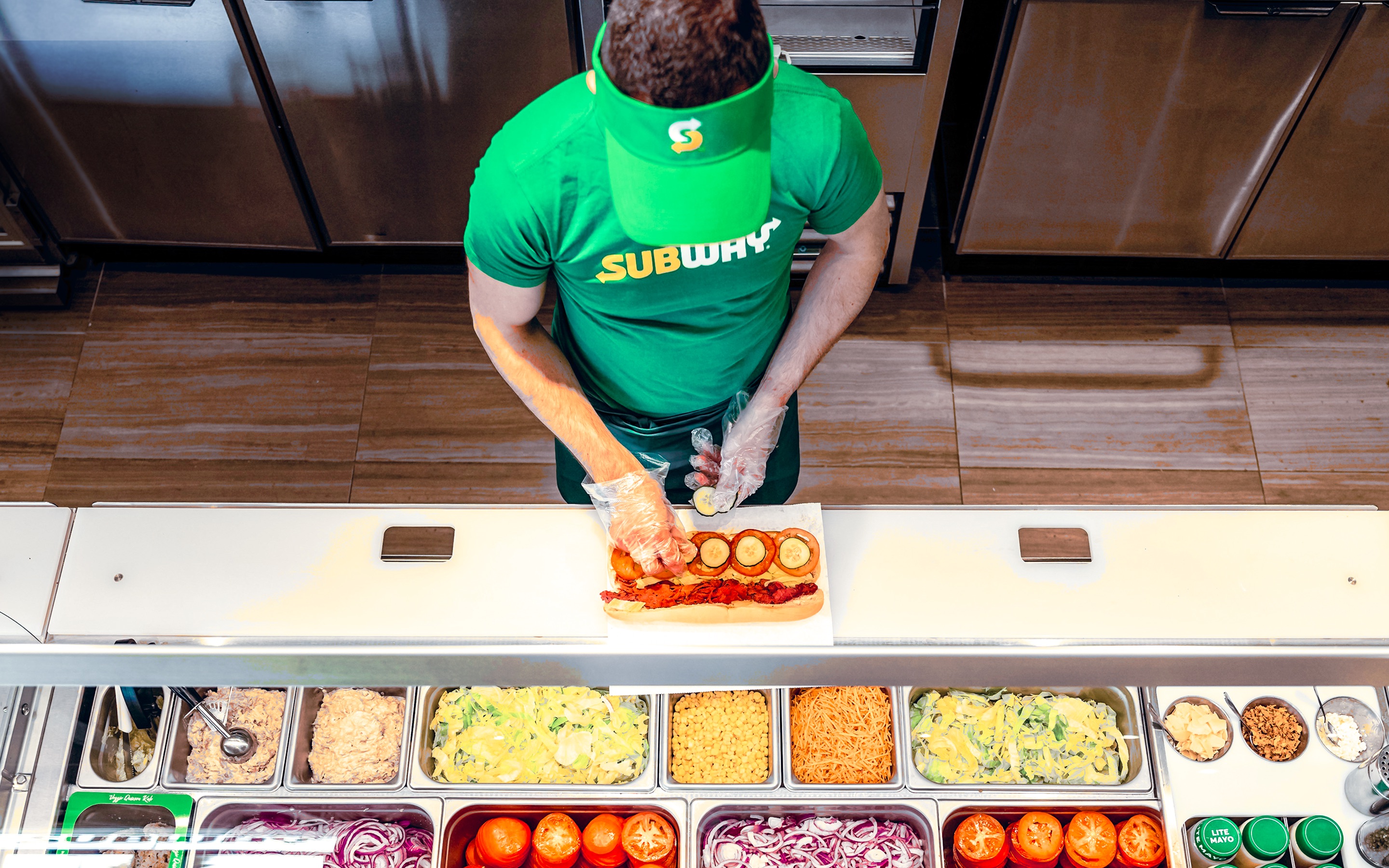 Subway sandwich artist preparing a custom order at the fresh ingredient line